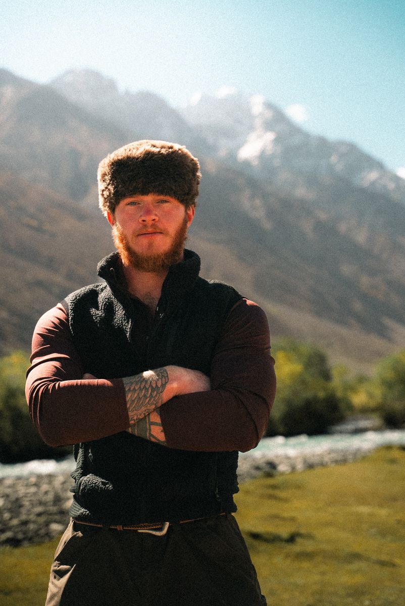 Portrait of Charlie Maughan, arms crossed, glacial river and mountains behind