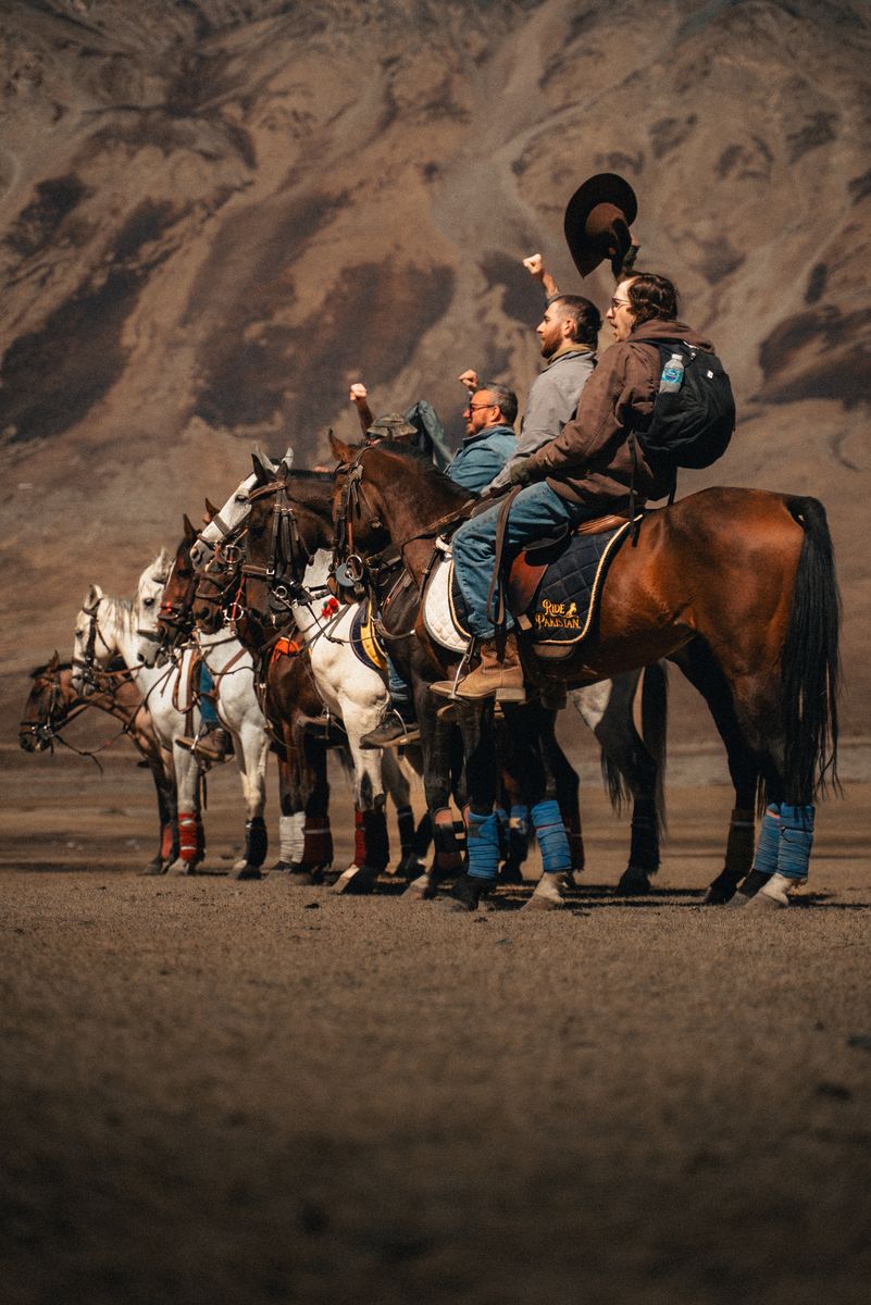 The Frontiersmen on horseback in a dry mountain valley, fists raised